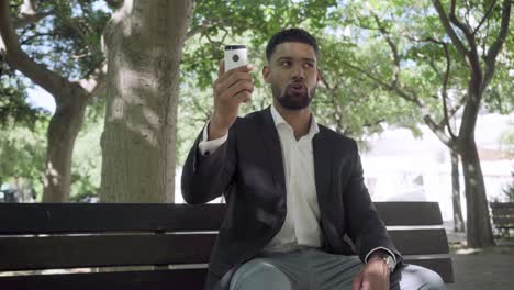 Confident-young-businessman-with-smartphone.sitting-on-bench